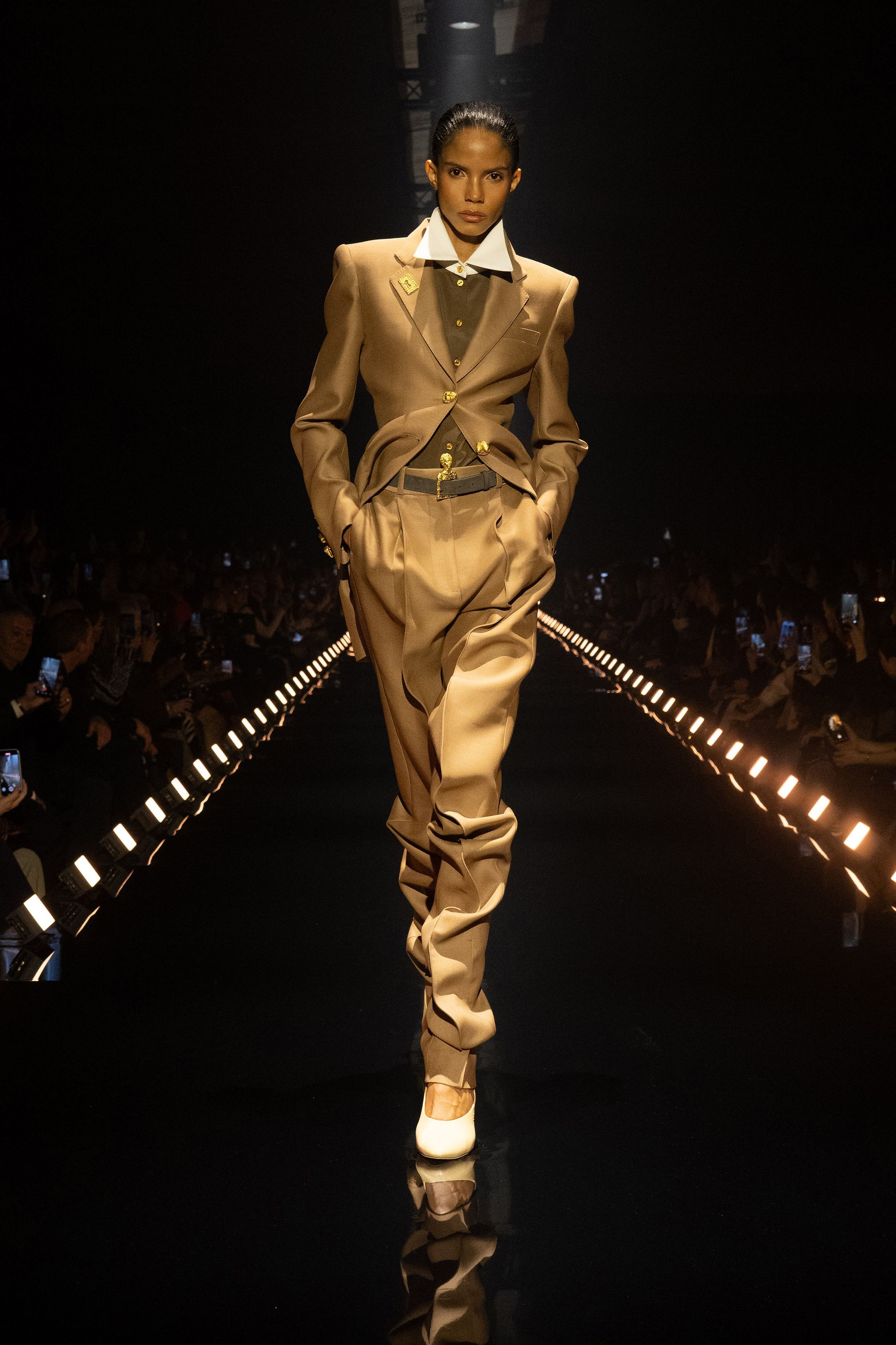 Schiaparelli 2026秋冬系列延续品牌标志性的超现实主义美学，在金色灯光的T台上呈现极具雕塑感的廓形。沙金色与黑金色成为主调，褶皱礼服、雕塑式西装与高腰裙装强化身体线条。经典的金属装饰、夸张肩线以及精致刺绣细节构成强烈视觉符号，使整场秀既华丽又充满戏剧张力。设计师通过结构与面料的张力对比，让高级定制的艺术精神融入现代女性衣橱-顽石频道趋势研究